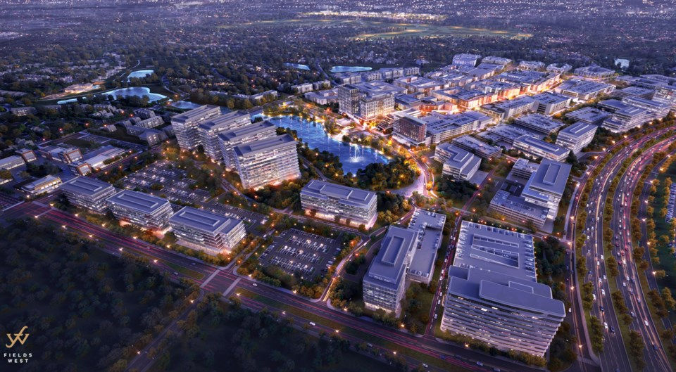 Aerial view of a sprawling, illuminated urban development with modern buildings, roads, and a central lake at dusk. Fields West logo visible.