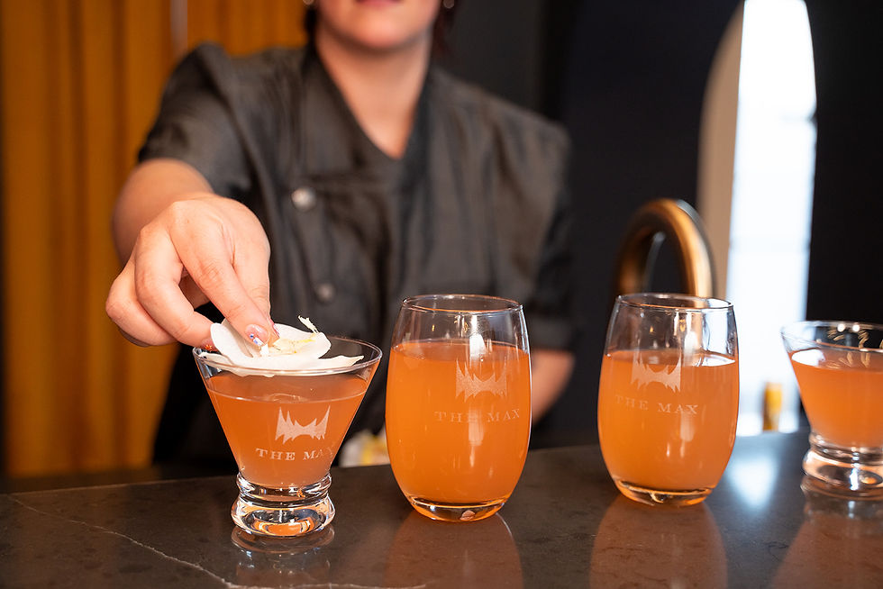 Bartender placing a floral garnish on a cocktail in front of a row of peach-colored drinks.