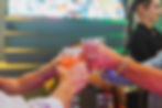 Group of people raising cocktails in a celebratory toast at a colorful bar