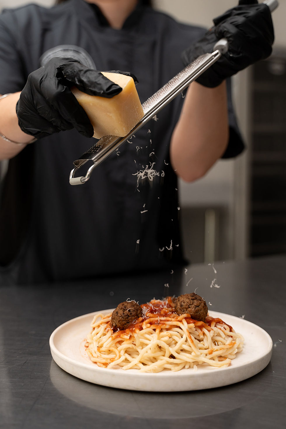 Chef grating cheese over a plate of spaghetti and meatballs in a professional kitchen, representing vendor food services.