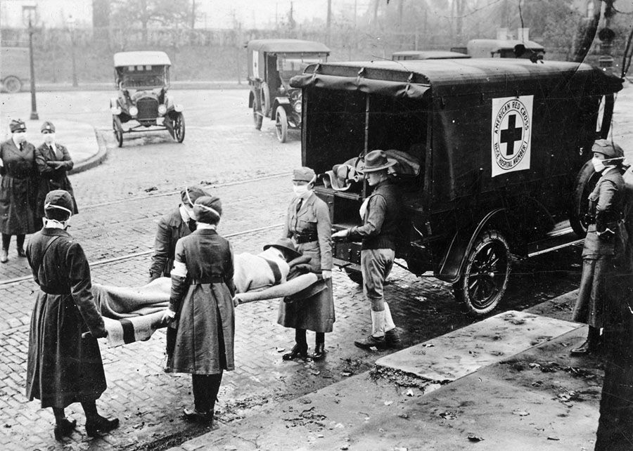 With masks over their faces, members of the American Red Cross remove a victim of the Spanish Flu from a house at Etzel and Page Avenues, St. Louis, Missouri, 1918. St. Louis Post Dispatch
