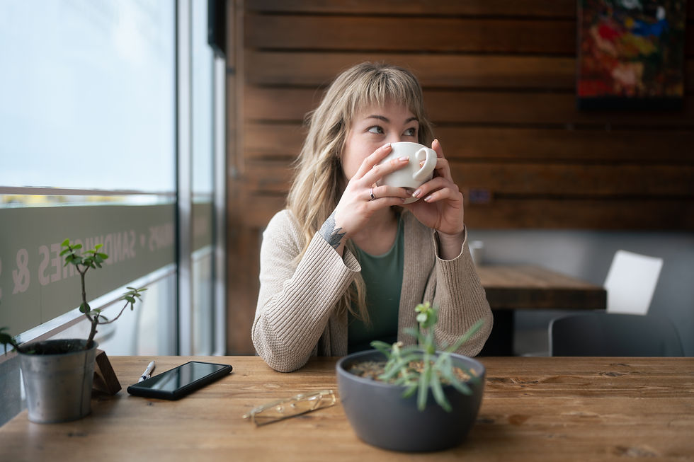 Wellness coach Meg. Woman drinking coffee at cafe with a plant.