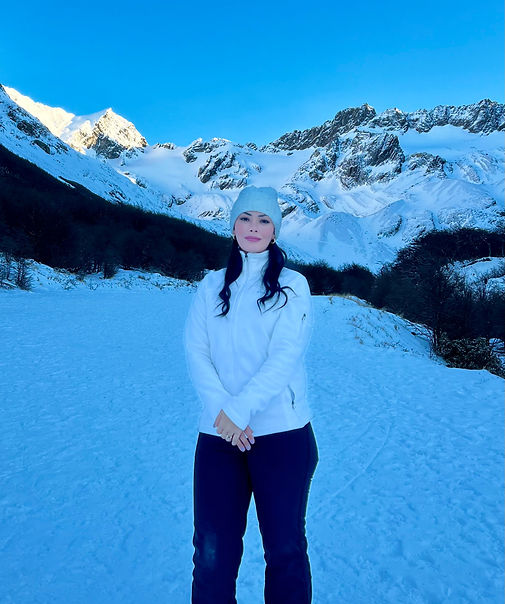 Bruna Freire tirando em uma paisagem nevada, usando um gorro branco decorado com pérolas.