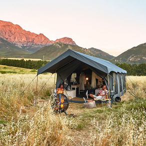 A photograph of a tented camp in a field against a mountain backdrop in South Africa.