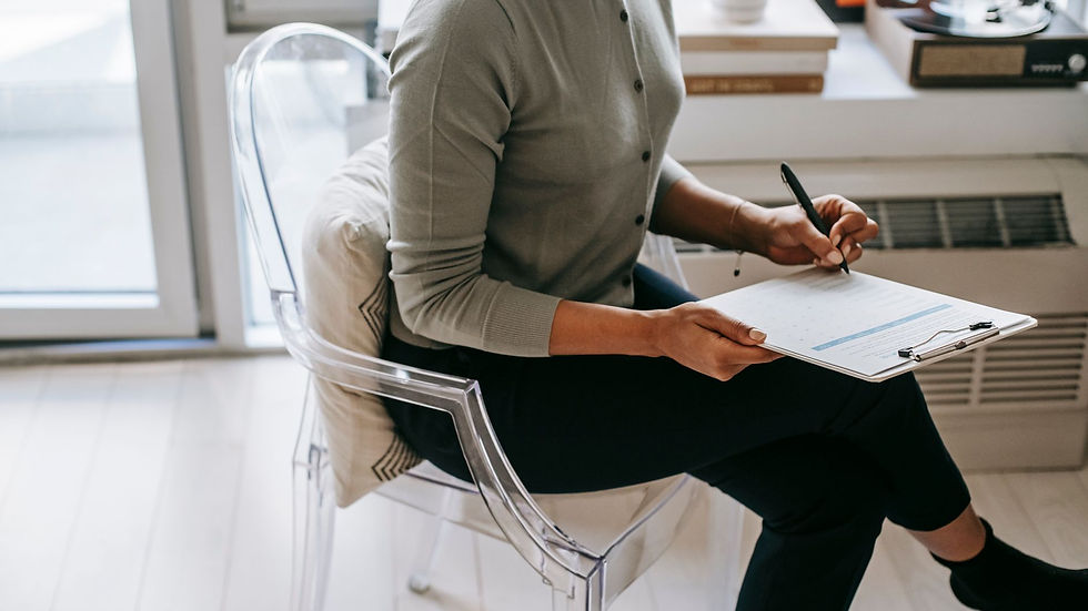 From above of unrecognizable female psychologist with crossed legs taking notes on clipboard while filling out questionnaire during psychotherapy appointment in cozy office