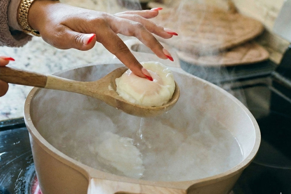 Hands with red nails hold a wooden spoon lifting a poached egg from a steaming pot in a kitchen setting. Eggs Benedict with Hollandaise sauce made by Nina Meek from Cozy Cooking By NIna