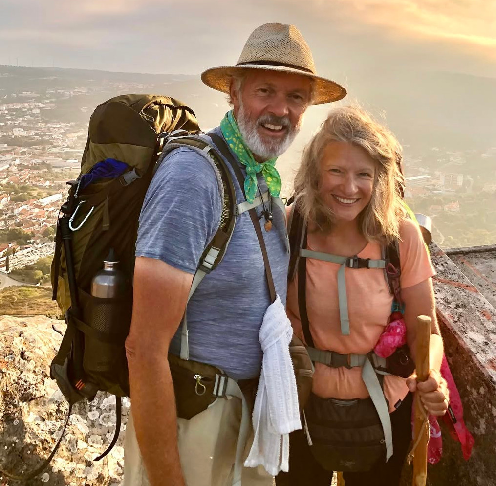 Kate and Robert walking the Camino de Santiago together, wearing backpacks in the evening light.
