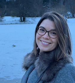 Nasmijana žena s naočalama u zimskom kaputu pored jezera.