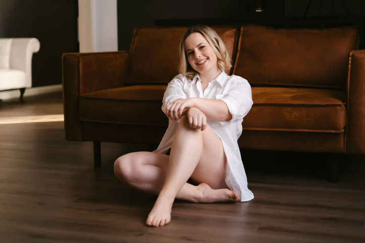 Lachende Frau in weißem Hemd sitzt vor dem Ledersofa, Boudoir Shooting in Wien