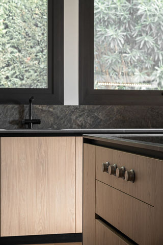 cuisine au design contemporain qui privilégie un équilibre raffiné entre les textures naturelles et industrielles. L’aménagement s’articule autour de l’utilisation de matériaux contrastés, mariant la chaleur organique du bois clair à la rigueur minérale de plans de travail en pierre sombre. La structure privilégie une ouverture sur l'extérieur, intégrant de larges fenêtres qui encadrent la végétation comme un élément décoratif à part entière. À travers ces différentes perspectives, l'œuvre souligne une esthétique de minimalisme sophistiqué où chaque détail fonctionnel s'efface derrière une harmonie visuelle apaisante.