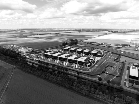 Aerial view of a large hyperscale data center campus surrounded by agricultural land and wind turbines, illustrating high-density digital infrastructure integrated with energy generation and rural land use.