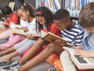 Young children seated on the floor in front of shelves of books at the library. They're all reading books