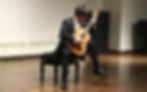 Peter Fletcher sitting on a piano bench playing a guitar