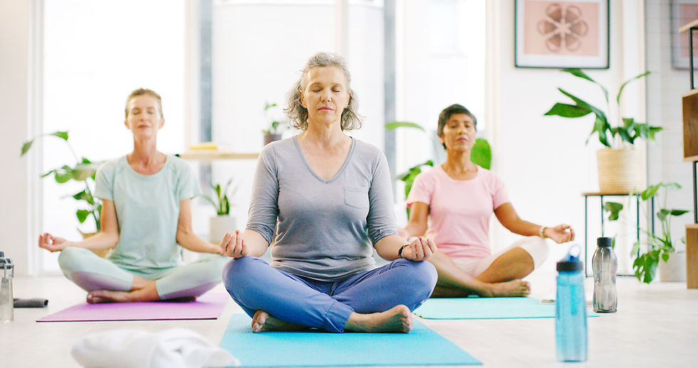 Group of 3 older women seated cross legged on a wooden floor during yoga class