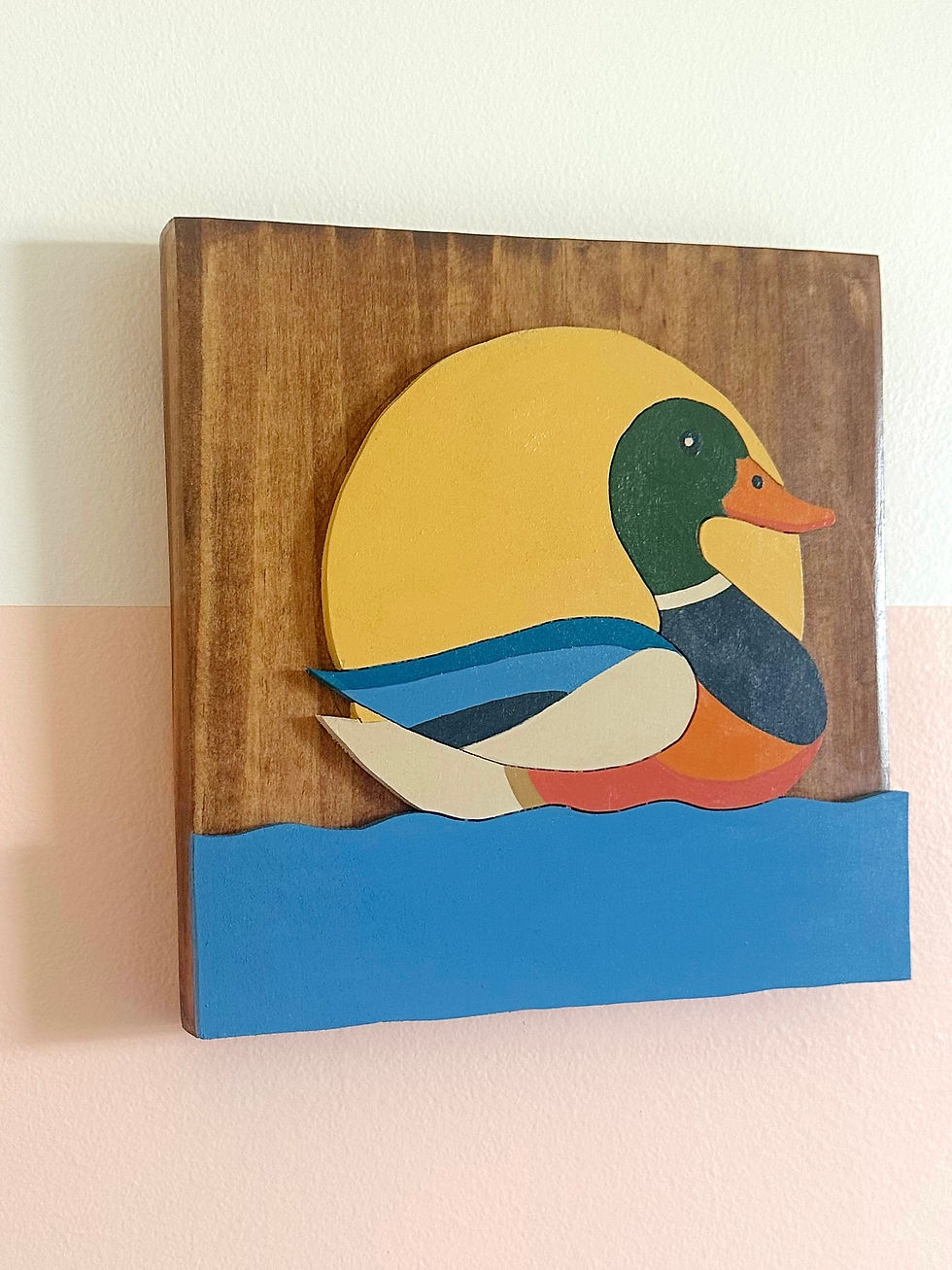 Thumbnail: Colorful wooden art featuring a mallard duck swimming against a yellow sun.