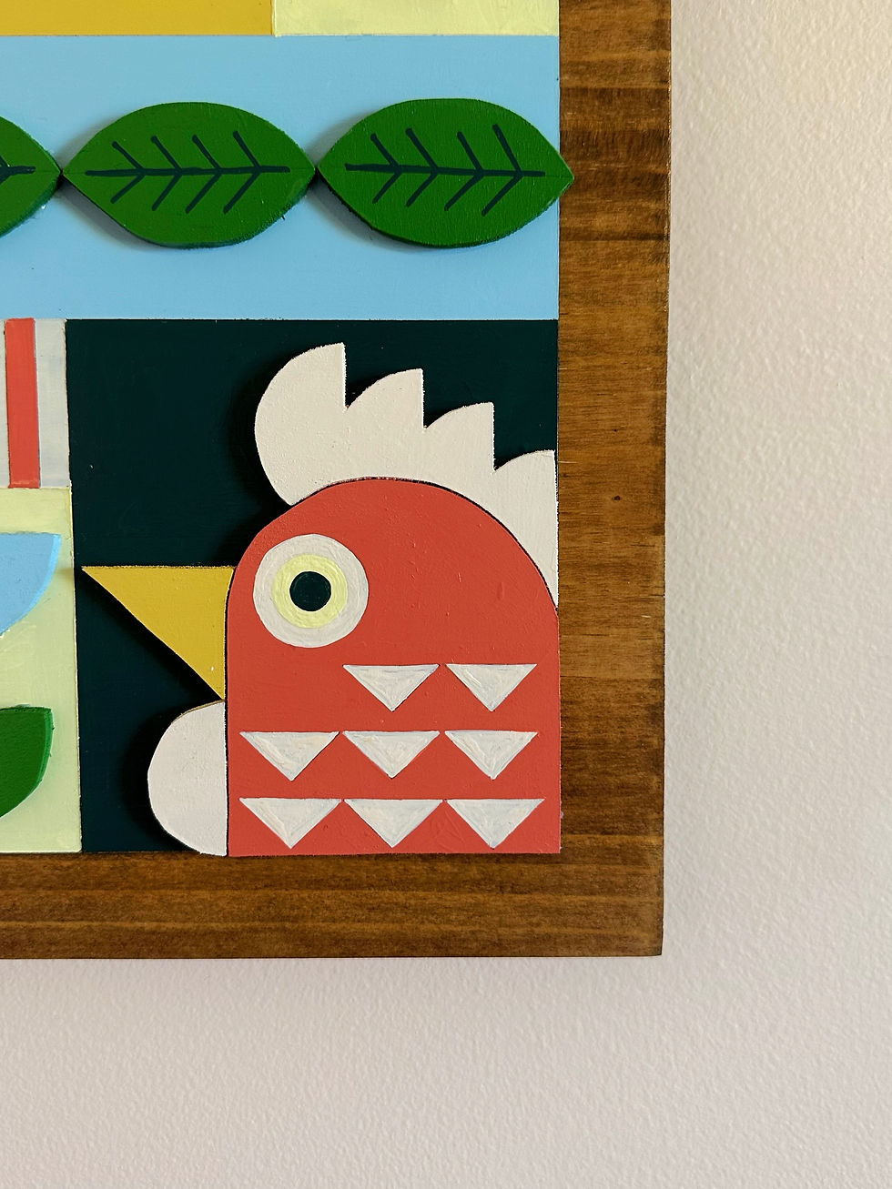 Stylized red rooster head in colorful block art with green leaves.