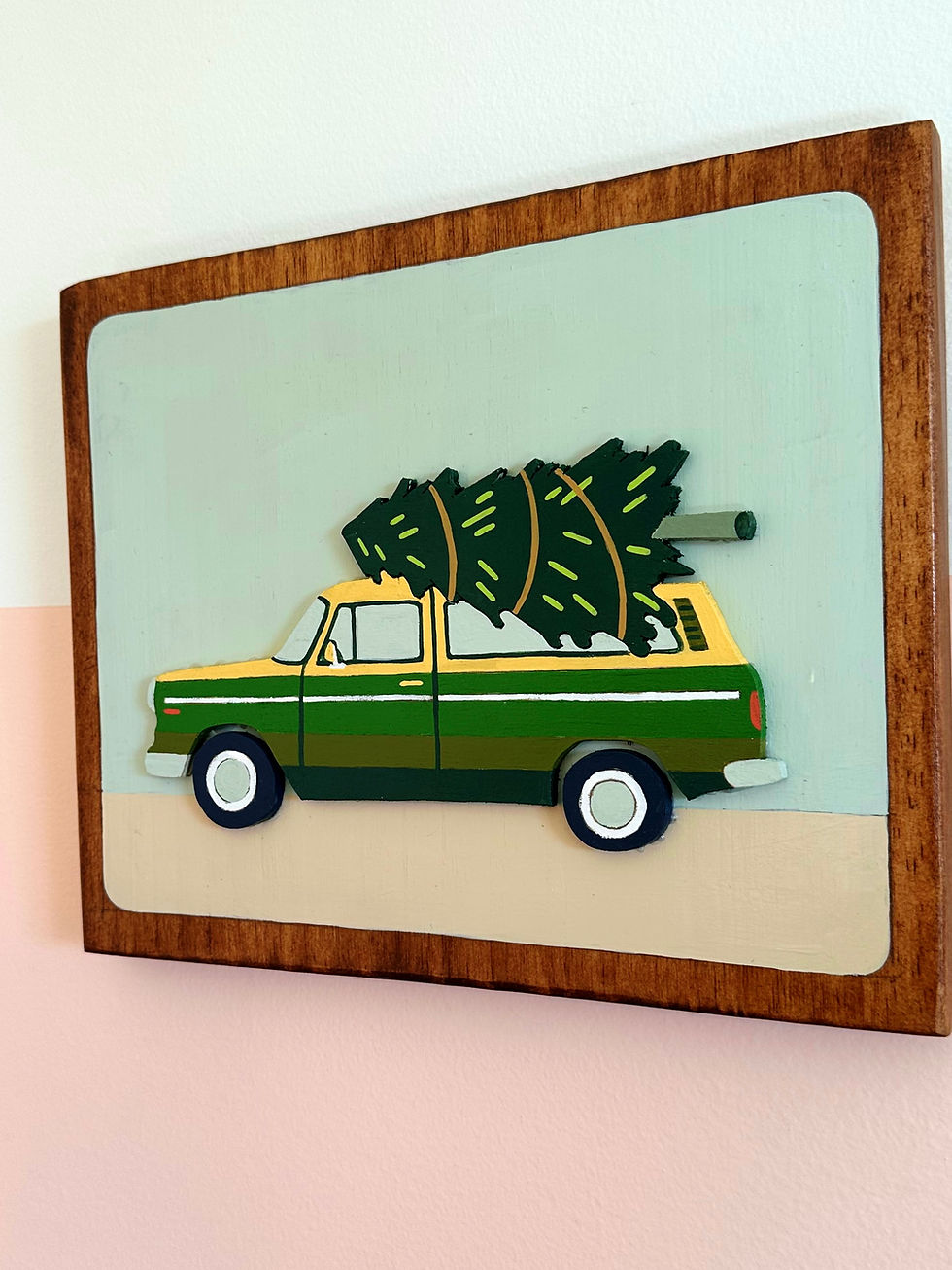 Thumbnail: Wooden sign features green station wagon carrying a Christmas tree.