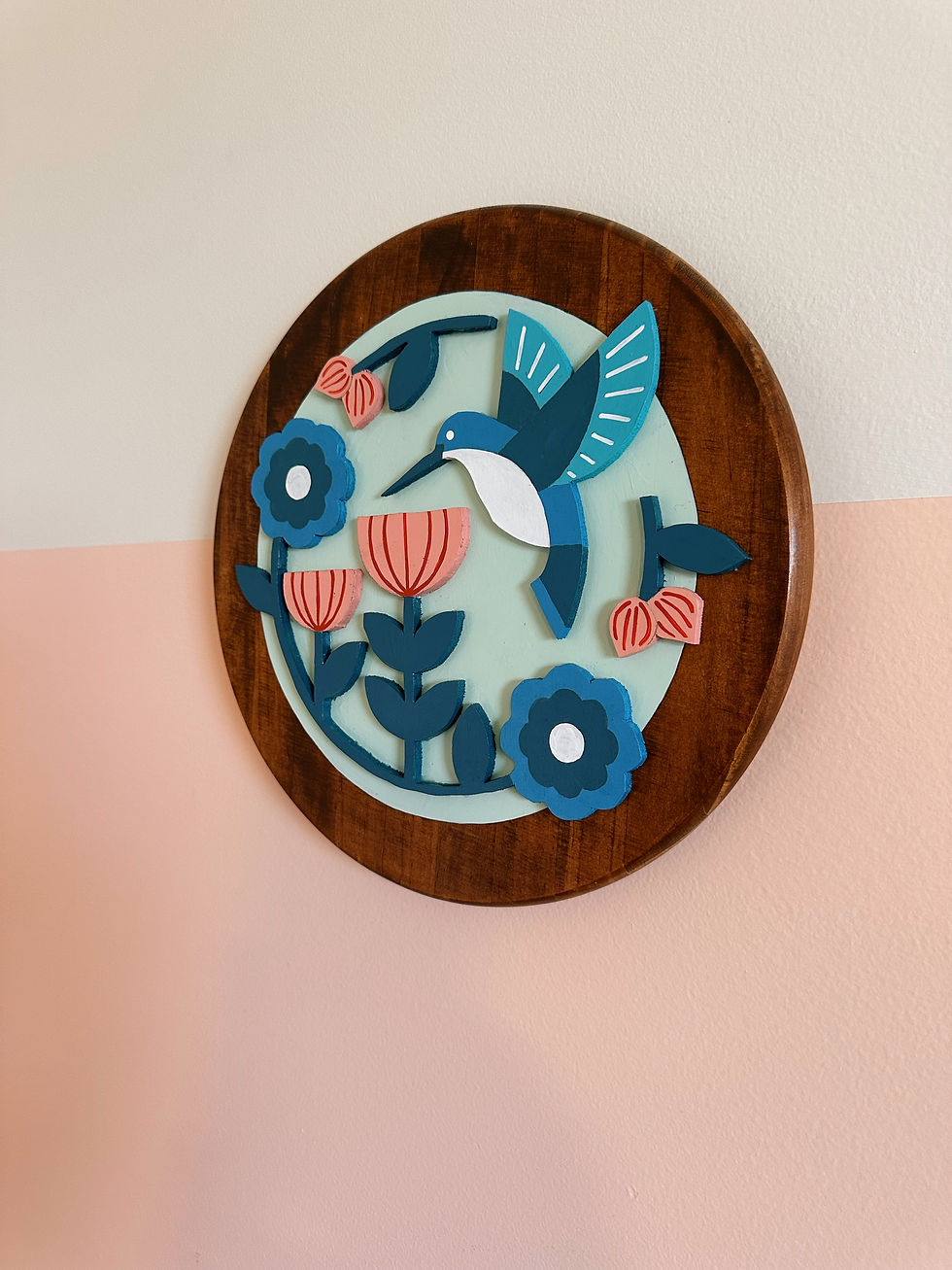 Round wooden wall art, blue hummingbird, coral flowers, cut-out style.