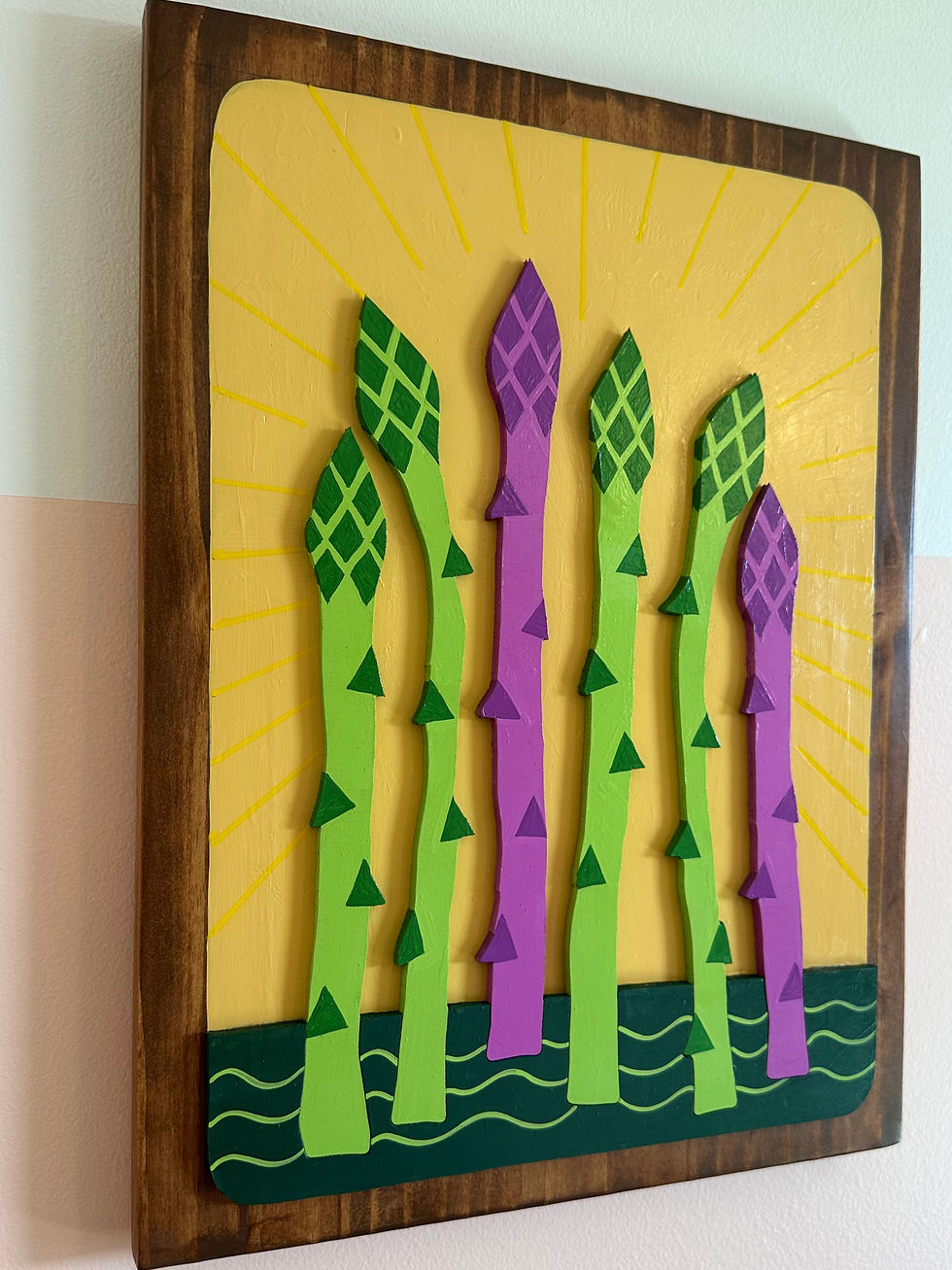 Thumbnail: Wooden plaque featuring green and purple asparagus on a yellow sunburst background.