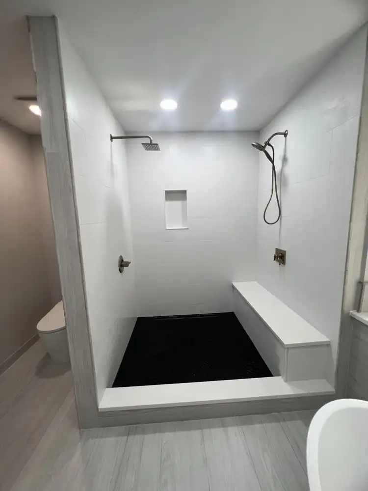 Walk-in shower with white large-format tile, black herringbone floor and quartz bench, Medina