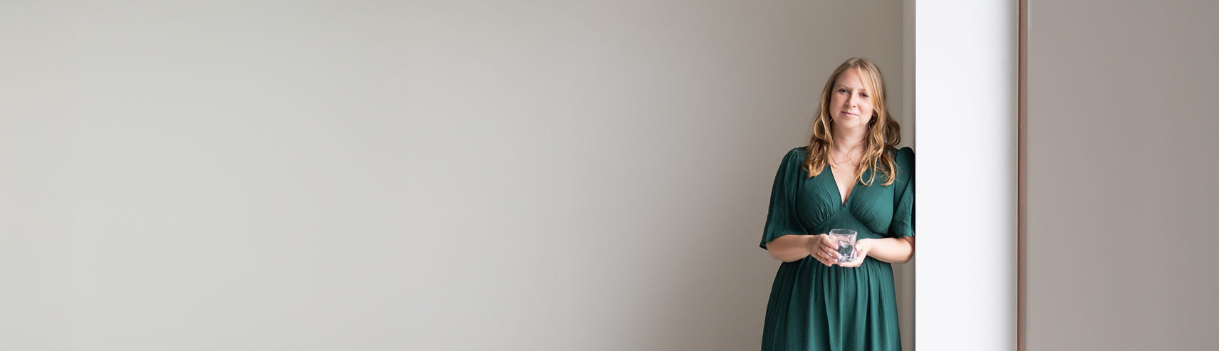 Vrouw in groene jurk staand bij raam met glas water – architect Lotte Holvoet