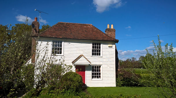 Applefield cottage, a white weatherboard listed building with a bright red front door.