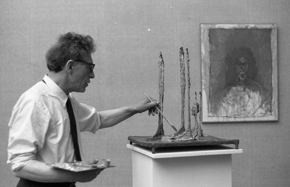 Artista dipingendo figura filiforme accanto ad altre, nel suo studio