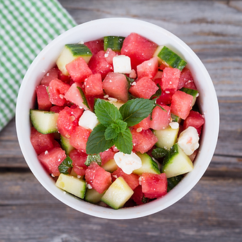 A bowl of watermelon, cucumber, feta, and mint salad on a wooden table with a green checkered napkin, creating a fresh summer vibe.