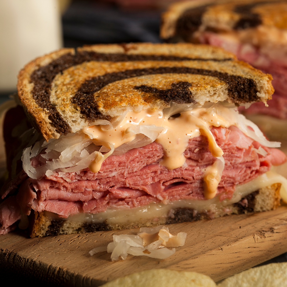Close-up of a Reuben sandwich with marbled rye bread, layered corned beef, sauerkraut, and melted cheese, dripping with Thousand Island dressing.