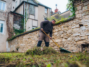 Etienne, de Grosset Paysages, ramasse de l'herbe et des feuilles mortes dans un jardin.