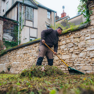 Etienne, de Grosset Paysages, ramasse de l'herbe et des feuilles mortes dans un jardin.