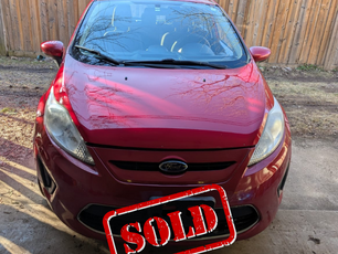 2011 Ford Fiesta SE in vibrant red, well-maintained and parked in a clean driveway. Sleek design with clear headlights, a bold front grille, and a smooth body. A great fuel-efficient compact car, perfect for city driving!