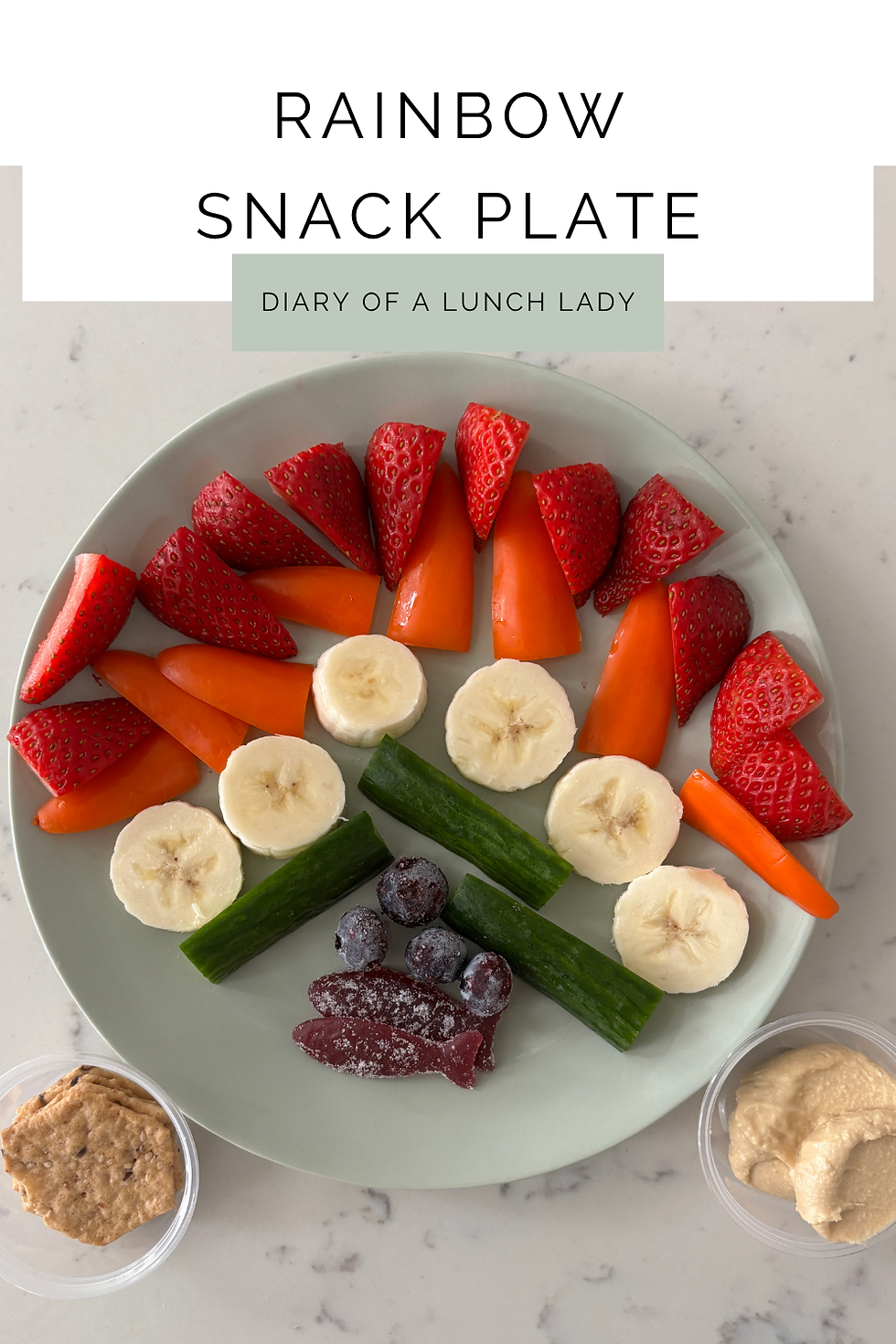 Rainbow snack plate with red strawberries, orange mini bell peppers, yellow banana slices, green cucumber sticks, frozen blueberries, and purple blackberry Swedish-style candy fish with crackers and hummus.