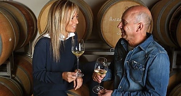 Winemakers Daniela and Luigi talking with white wine in their cellar 