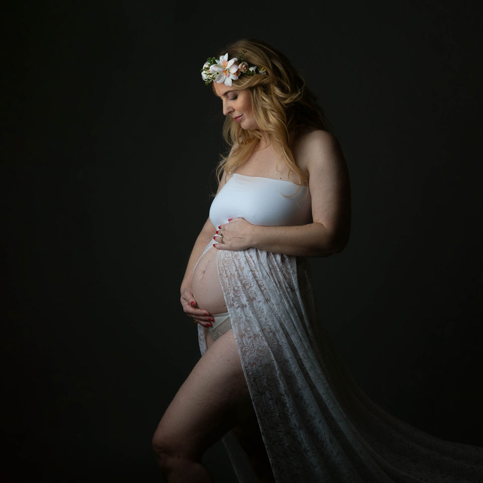 Pregnant woman in white lace gown, flower crown