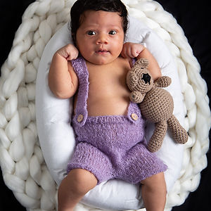 Adorable newborn baby boy in purple outfit, cuddling teddy bear