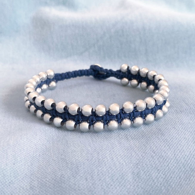 Hand-knotted bracelet with 925 sterling silver 5 mm beads and navy waxed cord on a soft blue background.