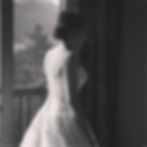 Bride in a white gown looking out a window.