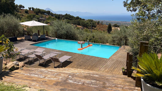 Private swimming pool with sun loungers, shaded seating and panoramic views of the Sicilian coast and Mediterranean Sea at Tenute Lomasi.