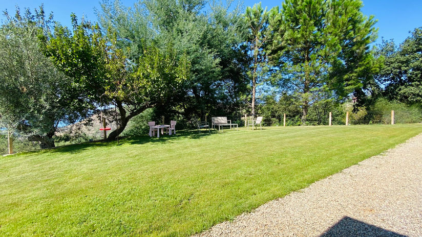 Spacious private garden with lawn, olive trees, outdoor seating and a children’s play area beside the covered patio at Tenute Lomasi.