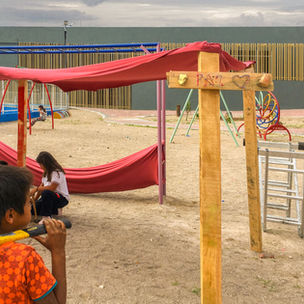 Niños construyendo una estructura de madera y tela en un parque con letrero que dice "Paz" y un corazón.