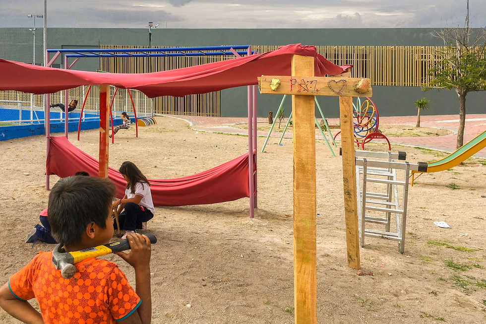 Niños construyendo una estructura de madera y tela en un parque con letrero que dice "Paz" y un corazón.