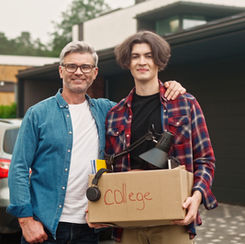 2 men standing outside in front of a car holding a box labeled "college"