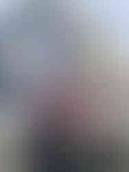 Three men stand in front of the statue of Billy Bremner at Elland Road, the home stadium of Leeds United. They are smiling and giving thumbs up, with one of them holding a Leeds United merchandise bag. Behind them, the stadium’s exterior is visible, including a large banner displaying "Leeds United" and the club’s crest, along with the slogan "Marching on Together." The statue is adorned with Leeds United scarves, and floral tributes are placed at its base. The scene captures a moment of joy and camaraderie outside the iconic stadium.