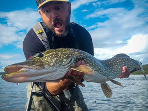 Angler holding a trophy northern pike caught near Fish'Home in Swedish Lapland, surrounded by pristine Scandinavian wilderness.