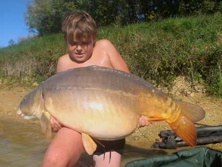 Grande carpe miroir capturée à l’automne lors d’un stage de pêche à la carpe sur un plan d’eau communal du Sud-Ouest, tenue dans l’eau par le moniteur.