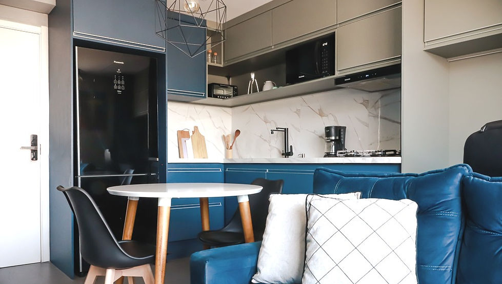 Cozinha integrada à sala de estar do Apartamento AV01, na Mooca, São Paulo, projetado pela GUZLIVE. O ambiente apresenta marcenaria azul e cinza, bancada com revestimento marmorizado, eletrodomésticos pretos, mesa de jantar redonda com cadeiras de design, pendente geométrico e sofá azul, combinando arquitetura contemporânea, funcionalidade e aproveitamento inteligente dos espaços.