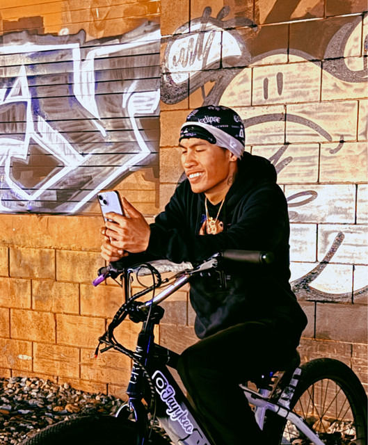 Wide-angle view of a rapper standing beside a bike near a San Diego park path at golden hour