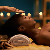 BIPOC person receiving a reiki treatment with their head on a towel and hands over their 3rd eye