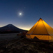 A golden-lit yert with a mountain and the moon in the background